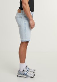 Világoskék farmer rövidnadrág, frayed szegéllyel és elhalványult textúrával, ezüst sportcipővel és fehér crew zoknival párosítva. A derékrészen látható bőr címke.