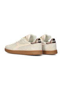 Beige suède sneakers met een crème accent en glanzende metallic details op de hak. Voorzien van een getextureerde rubberen zool en vetersluiting.