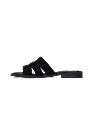Sandalias tipo "slide" de ante negro con suela plana. Presentan dos tiras anchas que se superponen y un adorno decorativo en la parte delantera. Diseño simple y minimalista.