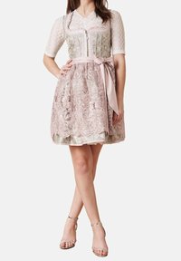 Vrouw in een knielange roze kanten jurk met bloemgeborduurd, een getailleerde bodice, korte mouwen, een strik in de taille en zilveren enkelbandhakken.