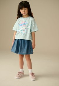 Ljusblå gingham kortärmad T-shirt med tecknad tryck, i kombination med en denimkjol och rosa sneakers, mot en neutral bakgrund.