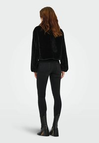 Zwarte nep bont cropped jas met lange mouwen, gecombineerd met hoge zwarte skinny jeans en zwarte hakken enkellaarsjes.
