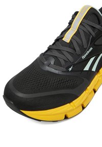 Must spordijalats võrguga ülaosaga, tekstureeritud viimistlusega, kollase keskosaga ja hallide detailidega. Varustatud paelte ja Reeboki logoga.