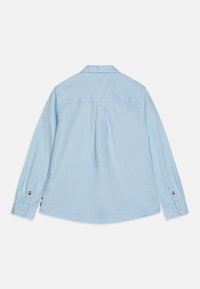 Camisa de manga larga azul claro con yugo trasero, dobladillo redondeado y puños abotonados, con acentos de logo en la manga. Tejido de algodón.