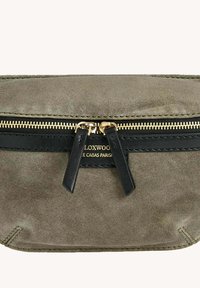Sac à main en suède gris avec des accents en cuir noir, comportant une fermeture éclair en or, des bandoulières détachables et un logo embossé. Texture lisse avec des détails de couture.