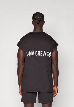 Mustata ilma varrukatega särk laia kaelusega, mille tagaküljel on valgete tähtedega trükitud "PUMA CREW '48". Kangas tundub sile ja kerge.