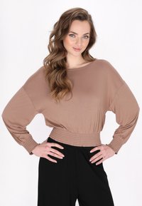 Maglia marrone a maniche lunghe con scollo a barca e vita elasticizzata, abbinata a pantaloni neri. Tessuto liscio, vestibilità comoda e polsini arricciati.