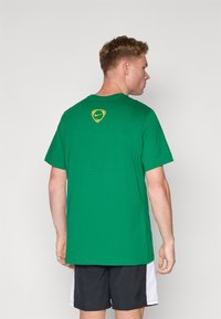 Grøn bomulds T-shirt med rund hals, korte ærmer og et gult Nike-logo på ryggen. Glat tekstur, afslappet pasform.