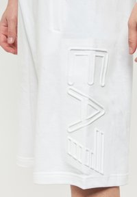 Shorts bianchi in cotone con un logo testurizzato in rilievo sul lato sinistro, dalla vestibilità comoda e con dettagli di orlo cucito.