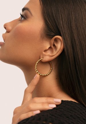 Boucles d'oreilles en or en forme de créole avec un design texturé comportant de petites perles sphériques uniformément espacées, portées à l'oreille, mettant en valeur leur forme circulaire.
