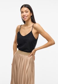 Čierny top s chevron vzorom a tenkými ramienkami skombinovaný s plisovanou, svetlo béžovou sukňou s širokým pružným pásom.