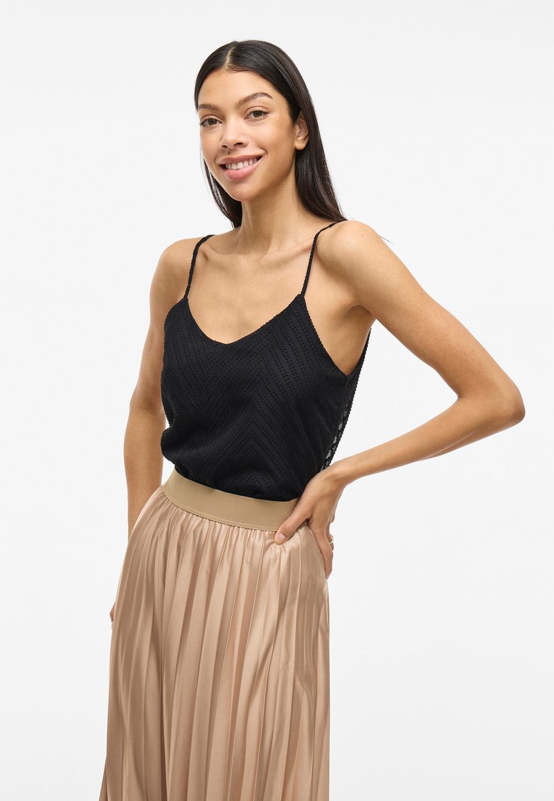 Čierny top s chevron vzorom a tenkými ramienkami skombinovaný s plisovanou, svetlo béžovou sukňou s širokým pružným pásom.