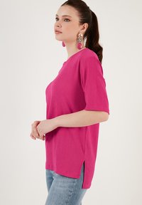Pink textured top with short sleeves, a rounded neckline, and side slits. Paired with light blue jeans, showcasing a casual look.