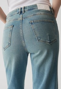 Jeans in denim azzurro chiaro presentano un design a vita alta, cinque tasche e una patch bianca con il marchio sulla cintura posteriore.