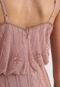 Pale pink dress featuring delicate beaded embellishments, sheer fabric, thin straps, and a zipper at the back with an elegant pattern.