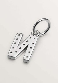 Charm de plata en forma de letra "N" con agujeros perforados, unido a un anillo circular. Superficie lisa y brillante con un diseño moderno.