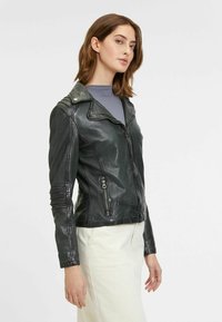 Zwarte leren motorjack met een nauwsluitend ontwerp, ritssluiting en diagonale zakken aan de voorkant. Voorzien van schouderepauletten en textuurdetails.