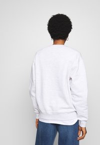 Světle šedá mikina s kulatým výstřihem, žebrovanými manžetami a lemem. Tkanina má texturu a působí neformálně, nošena přes bílý top.