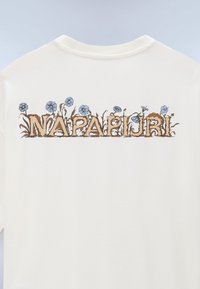 Άσπρο πουκάμισο πίσω με καφέ κείμενο "NAPAPIJRI", ενσωματωμένο με μπλε λουλούδια και πράσινους βλαστούς που μεγαλώνουν μέσα και γύρω από τα γράμματα.