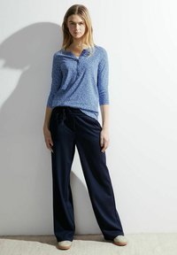 Niebieska bluzka w wzory z rękawami do trzech kwart z luźnymi granatowymi spodniami. Materiał wydaje się miękki i zwiewny, o swobodnym kroju.