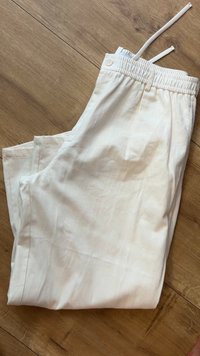 Vita linbyxor med en mjuk textur, elastisk midja, snörning och en enda knapp, vikt prydligt på en trä yta.