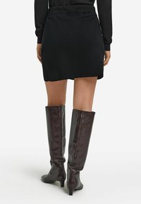 Schwarzer Strick-Minirock mit tailliertem Bund, kombiniert mit kniehohen, glänzenden dunkelbraunen Lederstiefeln mit mittelhohem Absatz.