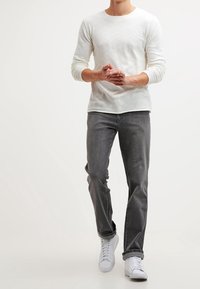 Ljust beige långärmad skjorta, grå jeans och vita sneakers. Slim fit. Skjortan har en mjuk textur, rund halsringning och subtila sömnadsdetaljer.