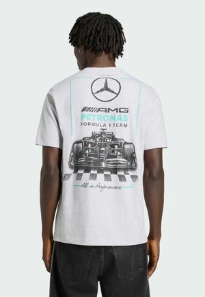 Mężczyzna z dredami noszący jasnoszary T-shirt zespołu Mercedes AMG Petronas Formula 1 z grafiką samochodu wyścigowego na plecach.