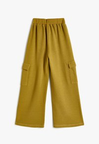 Senfgelbe weite Hosen aus weichem Stoff mit einem elastischen Bund und zwei seitlichen Cargo-Taschen. Flache Nähte und lockere Passform.