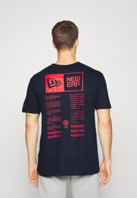 Námořnické bavlněné tričko s kulatým výstřihem. Červené akcenty zobrazují logo a text "NEW ERA" na zadní straně, zahrnující různé jazyky a designové detaily.