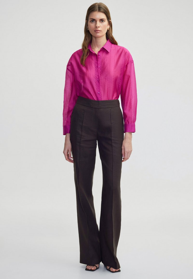 Fuchsia Hemd mit Knopfleiste aus transparentem Material, kombiniert mit braunen, hoch taillierten Schlaghosen. Einfaches Design, minimale Muster.