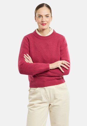 Pull en tricot rouge avec un col rond et des poignets côtelés, associé à un pantalon beige clair en tissu texturé et à coupe décontractée.
