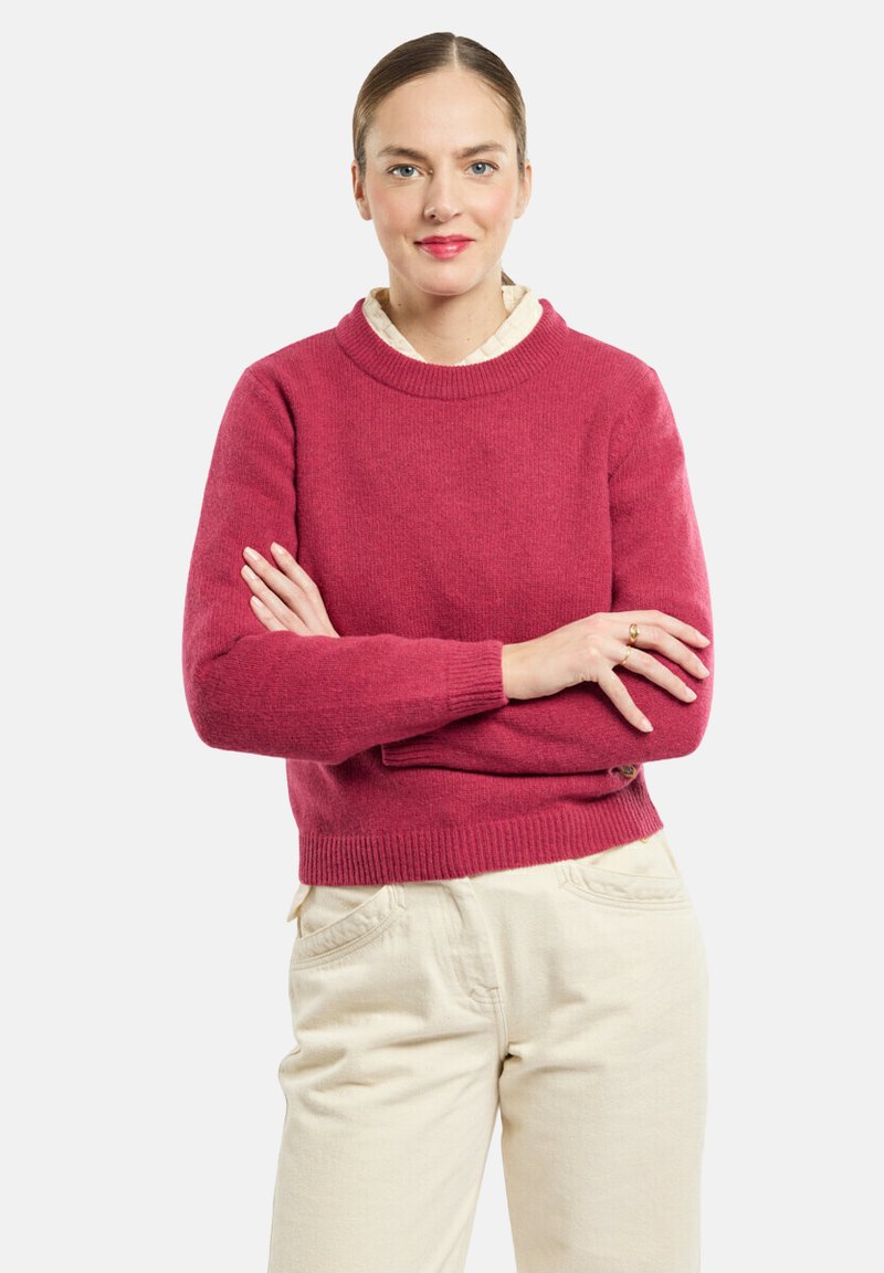 Maglione rosso a maglia con scollatura rotonda e polsini a coste, abbinato a pantaloni beige chiaro in tessuto strutturato e una vestibilità rilassata.
