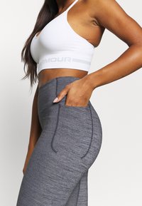 Sostenitore sportivo bianco con un ritaglio rotondo e logo grigio, abbinato a leggings grigi a vita alta con tasche e tessuto testurizzato.