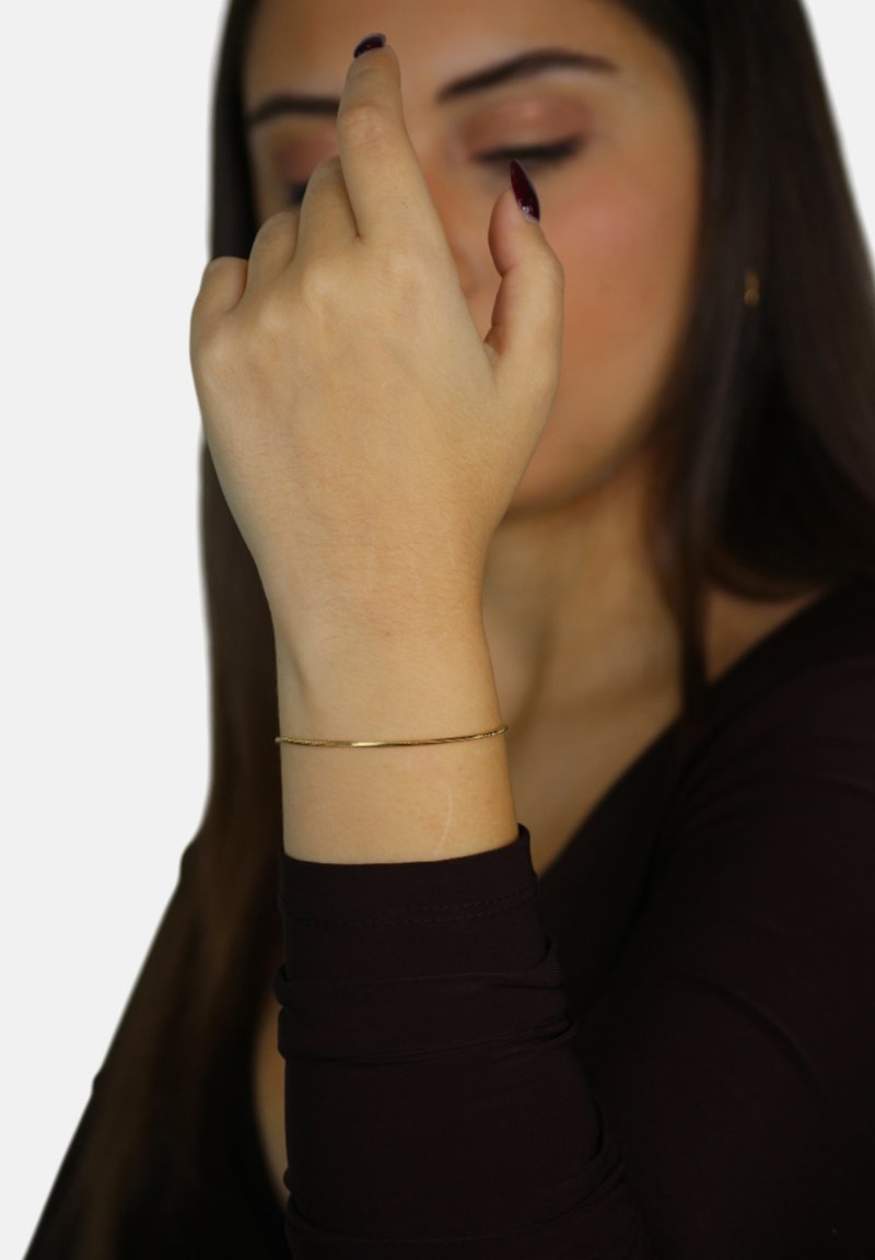 Bracciale in oro su un polso, con una finitura liscia e lucida. I gesti della mano indicano leggerezza ed eleganza.