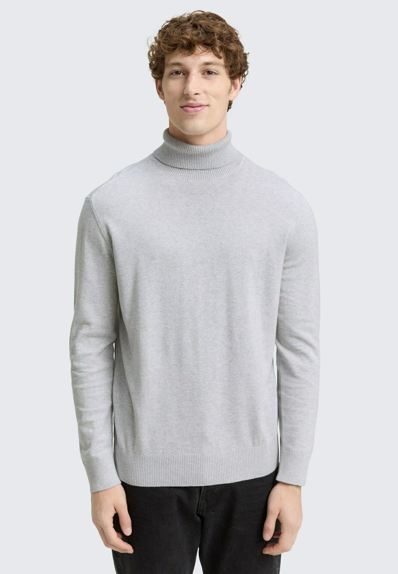 Hellgrauer Rollkragenpullover aus weichem Strick, mit langen Ärmeln sowie gerippten Bündchen und Saum. Das Model trägt ihn mit schwarzen Hosen.