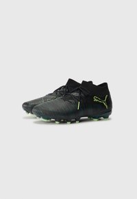 Black soccer cleats with a textured surface and green accent stripes. Features a high ankle collar and conical studs for traction.