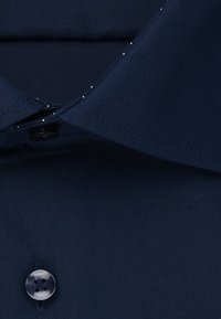Collo della camicia blu navy con dettaglio in bottoni. Tessuto liscio con una sottile texture e piccole macchie bianche a contrasto sul collo interno.