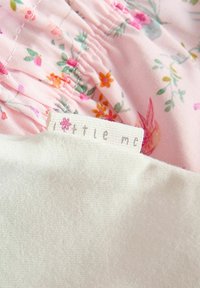 Tissu rose à motif floral avec texture froncée ; tissu de couleur crème en dessous avec une étiquette portant la mention "little me", mise en valeur par une petite fleur.
