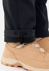 Zwarte broek met een fleece-gevoerd manchet, aangesnoerd met een toggle, gecombineerd met lichtbruine wandelschoenen met beige accenten en een gestructureerde zool.