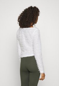 Tjock vit kortärmad tröja med långa ärmar, rund halsringning och strukturerad yta, i kombination med mörkgröna tajta leggings.