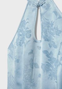 Haut sans manches bleu clair avec motif floral en relief et fermeture boucle nouée au niveau de l'encolure.
