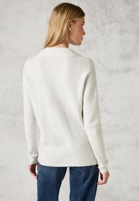 Pull en maille couleur crème avec un design texturé en nid d'abeille. Il présente des manches longues et une coupe décontractée, associé à un pantalon bleu foncé.