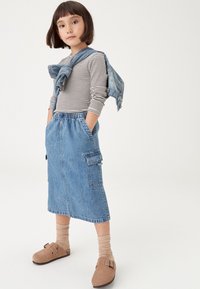 Džinsa svārki ar elastīgu vidukļa jostu, sānu kabatām un taisnu piegriezumu. Kombinēti ar svītrainu garroku topu un džinsa jaku. Brūnas slip-on kurpes.