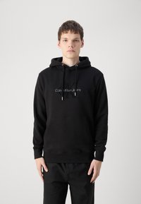 Zwarte hoodie met een kangoeroezak, trekkoorden en geborduurd "Calvin Klein Jeans" logo op de borst. Zacht materiaal, losse pasvorm.