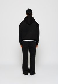Sweat-shirt à capuche noir avec une coupe décontractée, associé à un jeans en denim foncé. Le sweat-shirt a une grande capuche et des poignets côtelés.