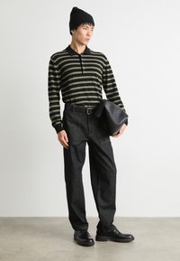 Polo cu dungi negre și oliv, cu mânecă lungă, purtat cu pantaloni din denim închis. Modelul ține o geantă din piele neagră; îmbrăcămintea are un design casual.