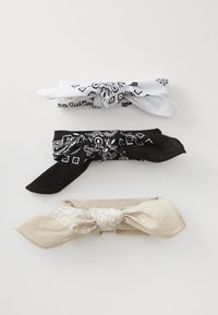 Three bandanas stacked: white with black patterns, black with white patterns, and beige with white designs. All are tied in knots.