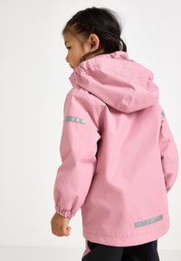 Rosa vattentålig jacka med huva, elastiska muddar och reflekterande detaljer på ärmarna och bak. Slät textur, avslappnad design.