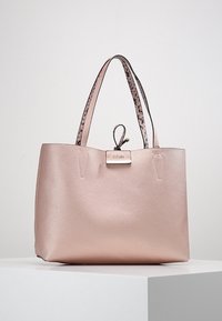 Torba tote w kolorze różowego złota, wykonana z teksturowanej skórki syntetycznej, z podwójnymi uchwytami w różnorodne wzory oraz metalową płytką logo. Przestronny, minimalistyczny design.
